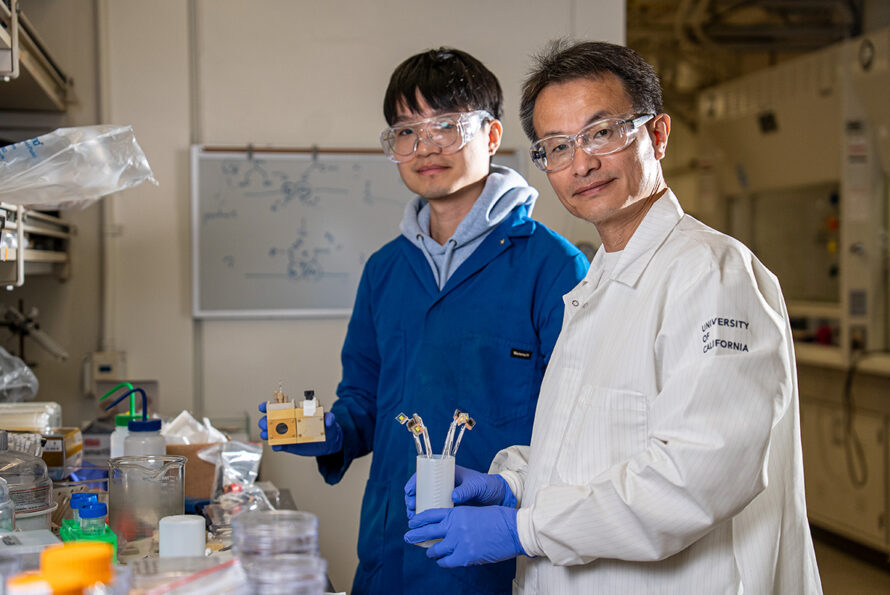 Two researchers posed to the right of a lab bench with various scientific instruments.